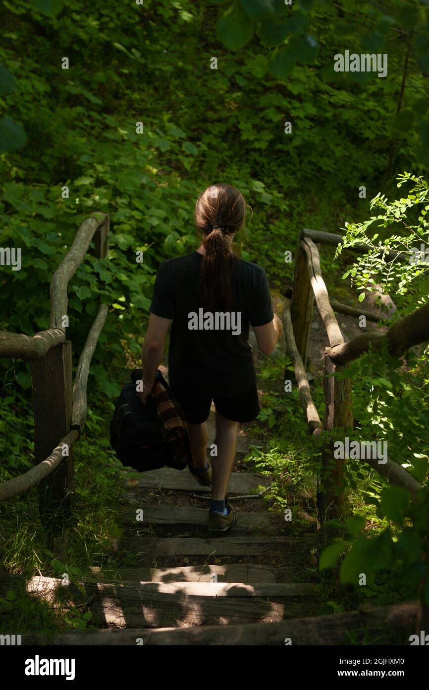 Man walking down the stairs in the forest | Back view photo from above of a person going down the stairs in the woods Stock Photo