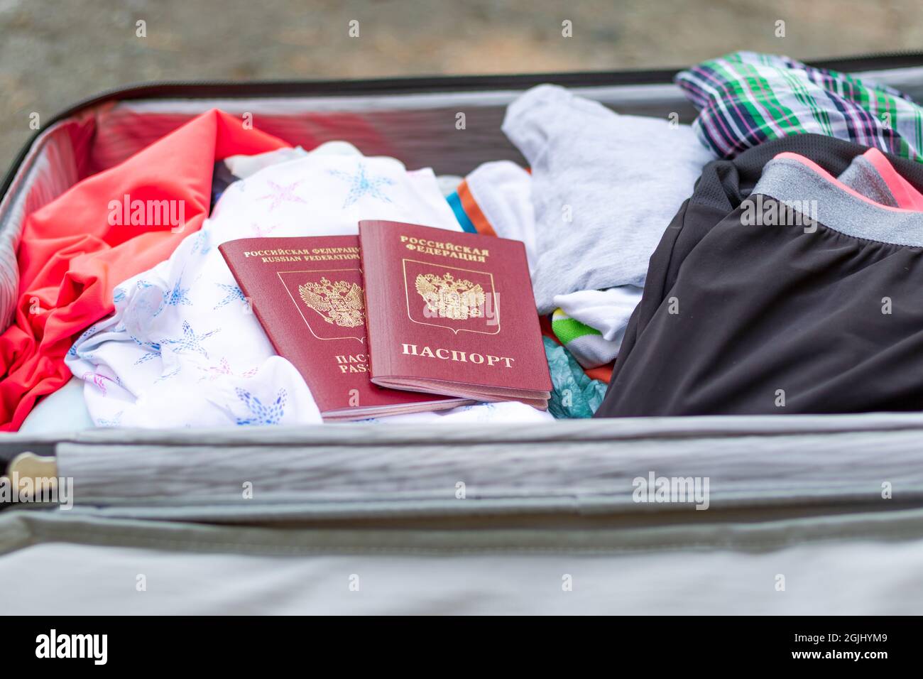 An open suitcase with things and two passports lies on the road on a sunny summer day. Selective focus Stock Photo