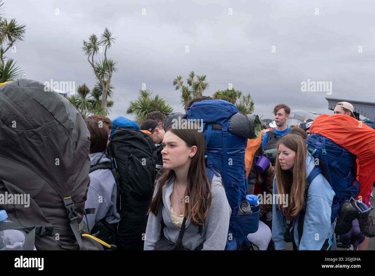 Young people carrying heavy rucksacks queueing for buses to take them to the opening day of The Boardmasters Festival in Cornwall. Stock Photo