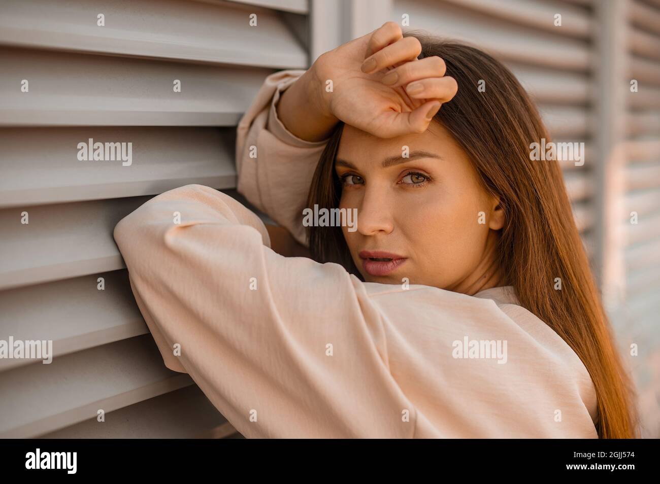 A picture of a young pretty woman in beige near the wall Stock Photo