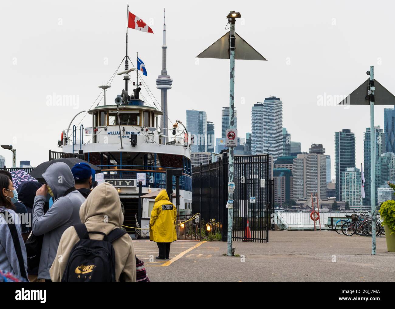 Toronto, Ontario, Canada - July 31 2021: Selective rear-view focus on woman security guard in yellow jacket facing a ferry on dock of Toronto Islands. Stock Photo