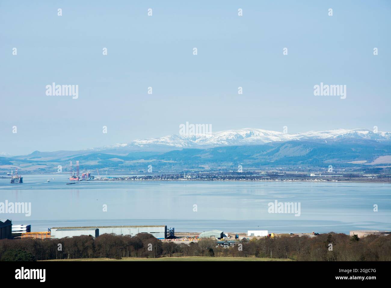 Imposing snow covered Ben Wyvis towers over the small town of Invergordon, nestled on the short of the inner Cromarty Firth in the Scottish Highlands Stock Photo