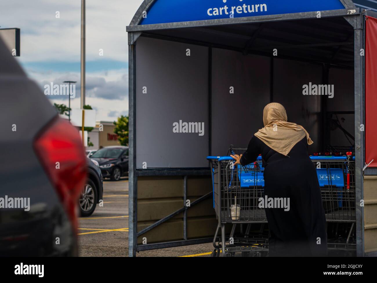 Toronto, Canada, June 2021 - Woman of islamic faith wearing headscarf returns a shopping cart to the bay in the parking lot Walmart Stock Photo