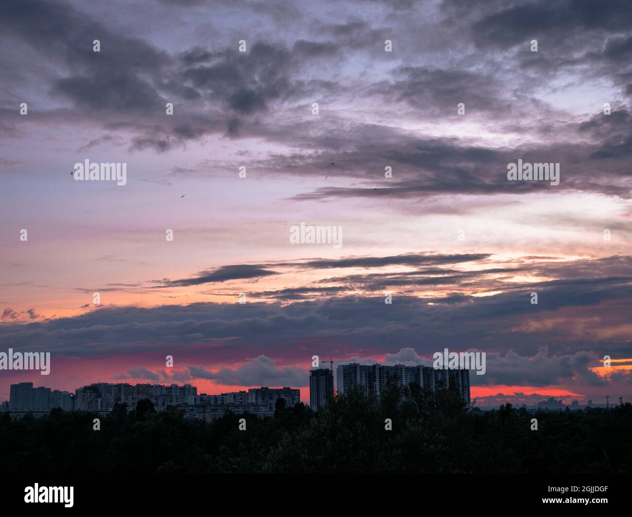 Colorful sunset over Kyiv (Kiev) city with buildings on the horizon. Industrial cityscape against backdrop of setting sun with red and lilac scenic. Stock Photo