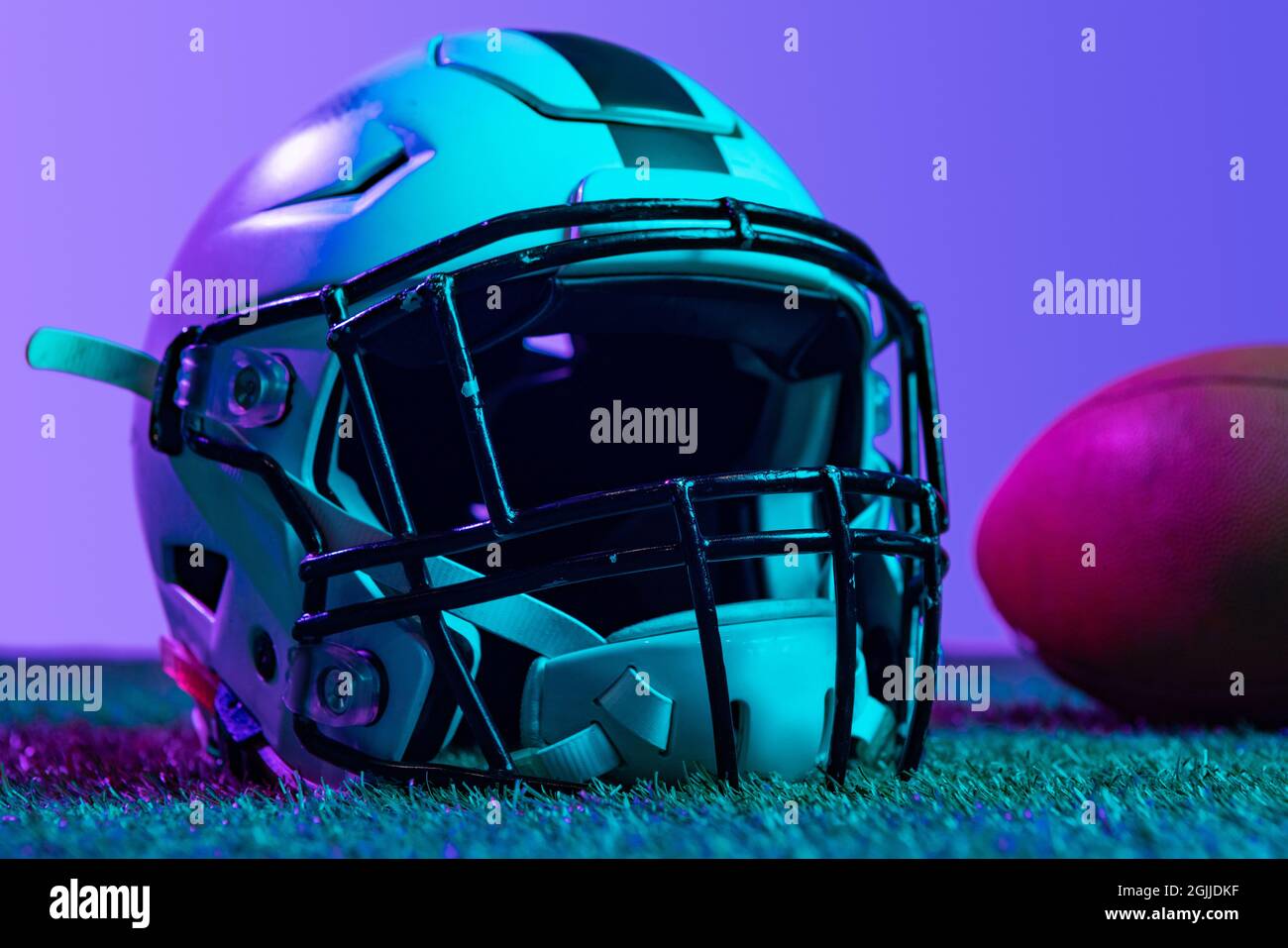best football helmet background neon Studio close-up shot of professional equipment for american football game  isolated over purple background in neon lights. Helmet and ball Stock Photo