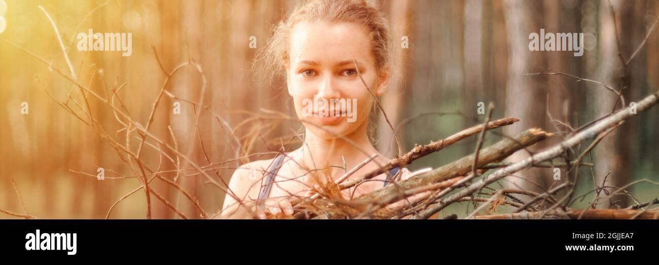 teenage girl with pimple skin collect branches firewood for campfire while traveling through summer forest nature. happy people survivalist traveler a Stock Photo