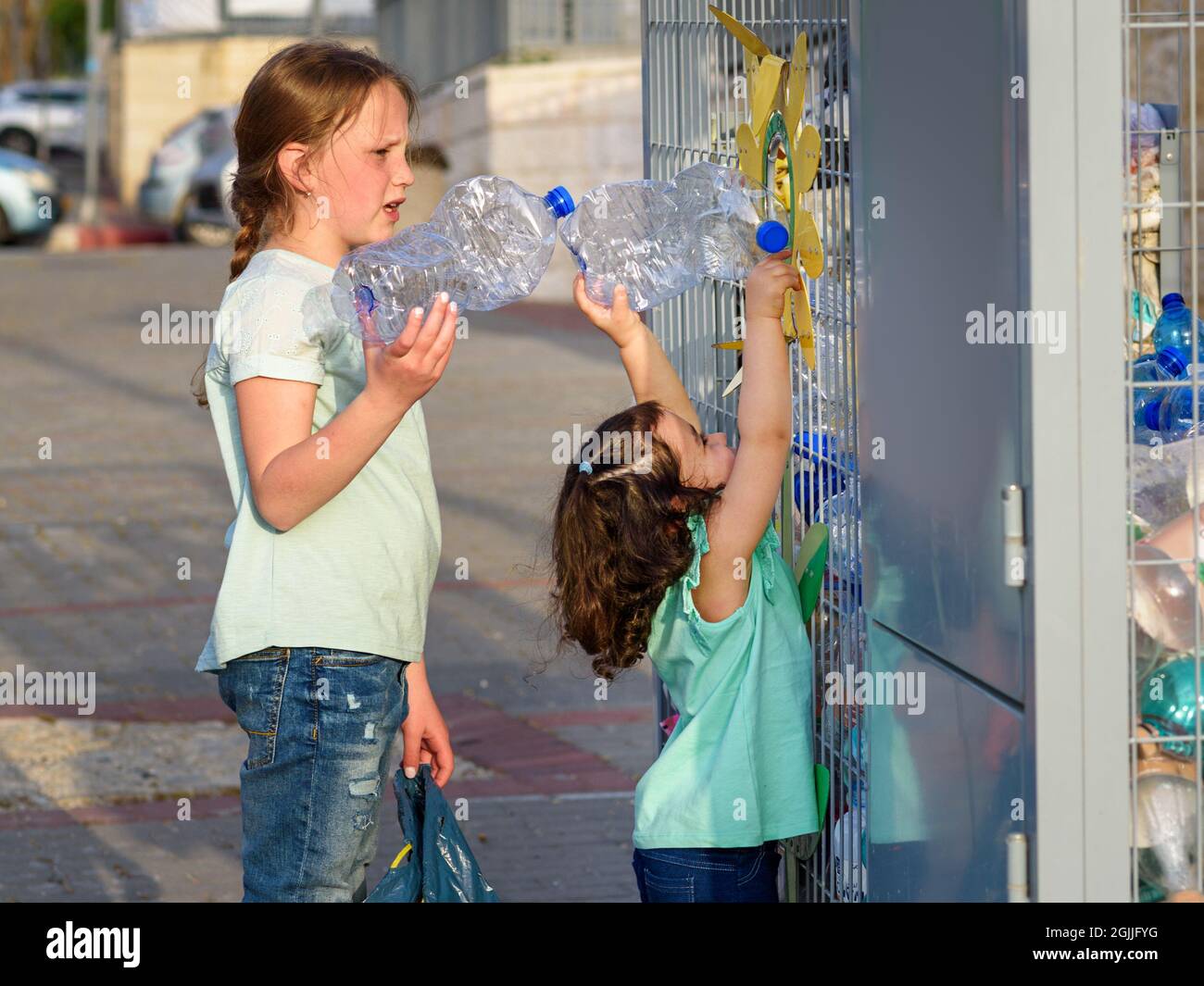 Little Girls Recycling Plastic Water Bottles In Yellow Metal Recycling