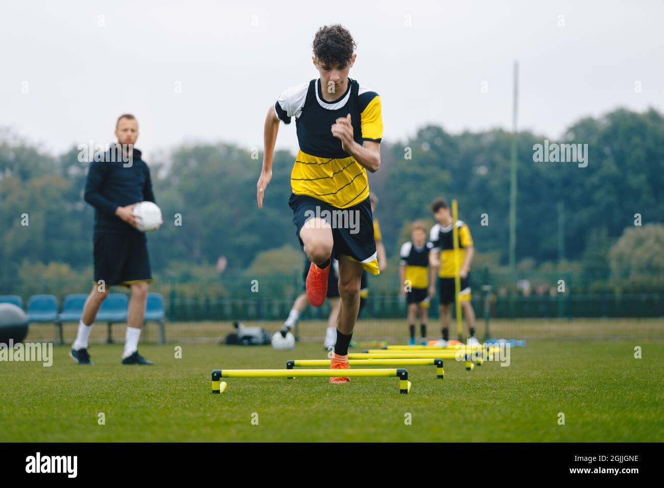 Junior soccer player running fast and ladder skipping. Boys practice football witch young coach. Teenagers on soccer training camp. Youth athletes imp Stock Photo