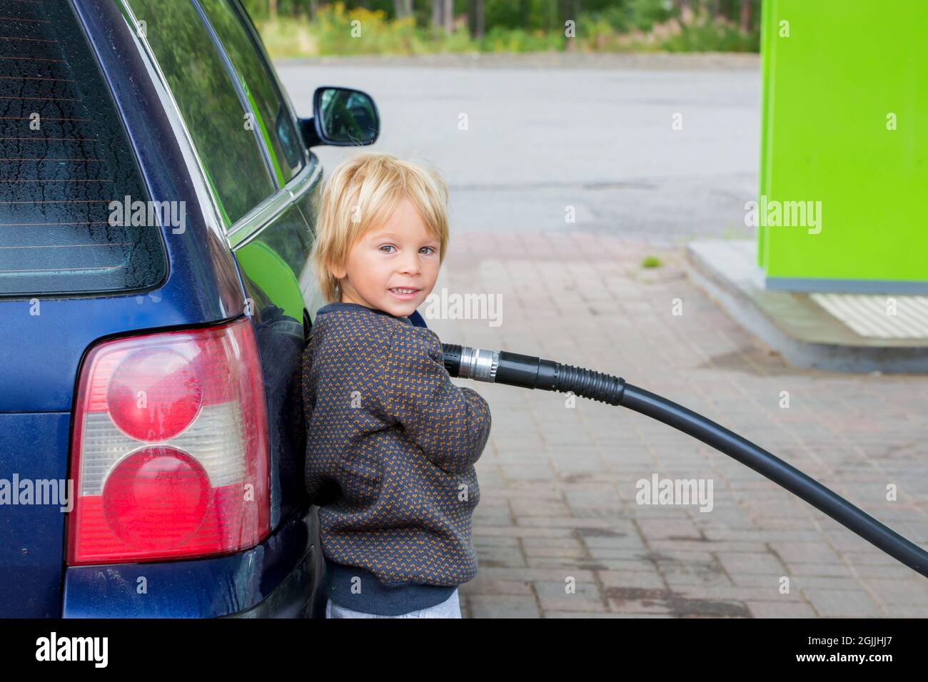 Sweet little child, blond boy, helping parents to put fuel in the car