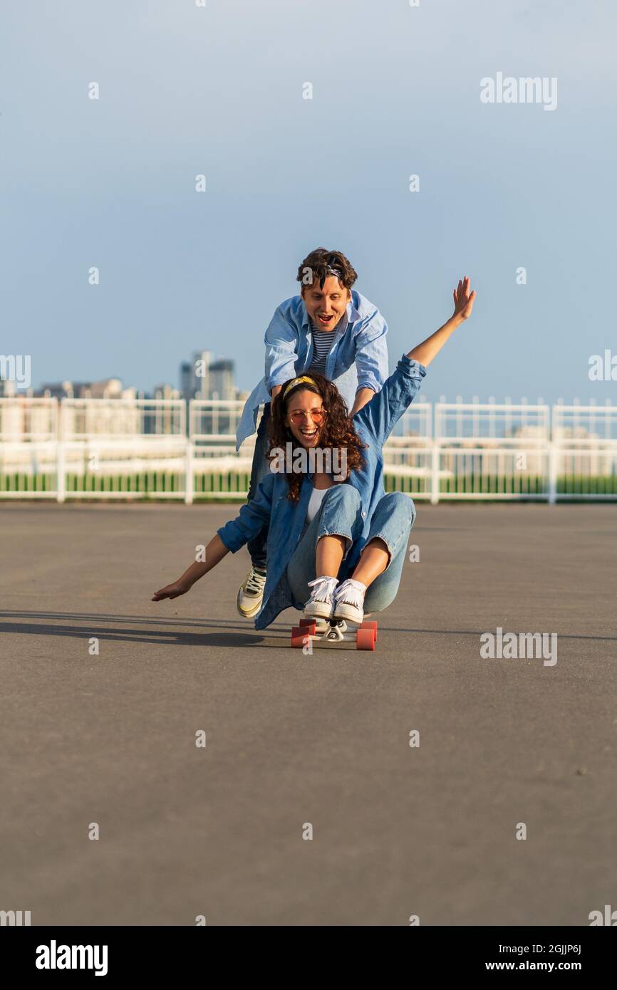 Young couple enjoy skateboarding together on street. Hipster man push back of woman sit on longboard Stock Photo