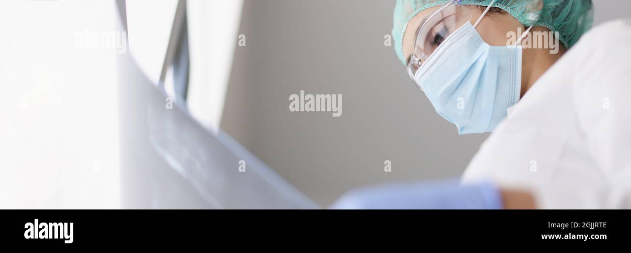 Doctor wearing protective mask and gloves examines an X-ray image Stock Photo