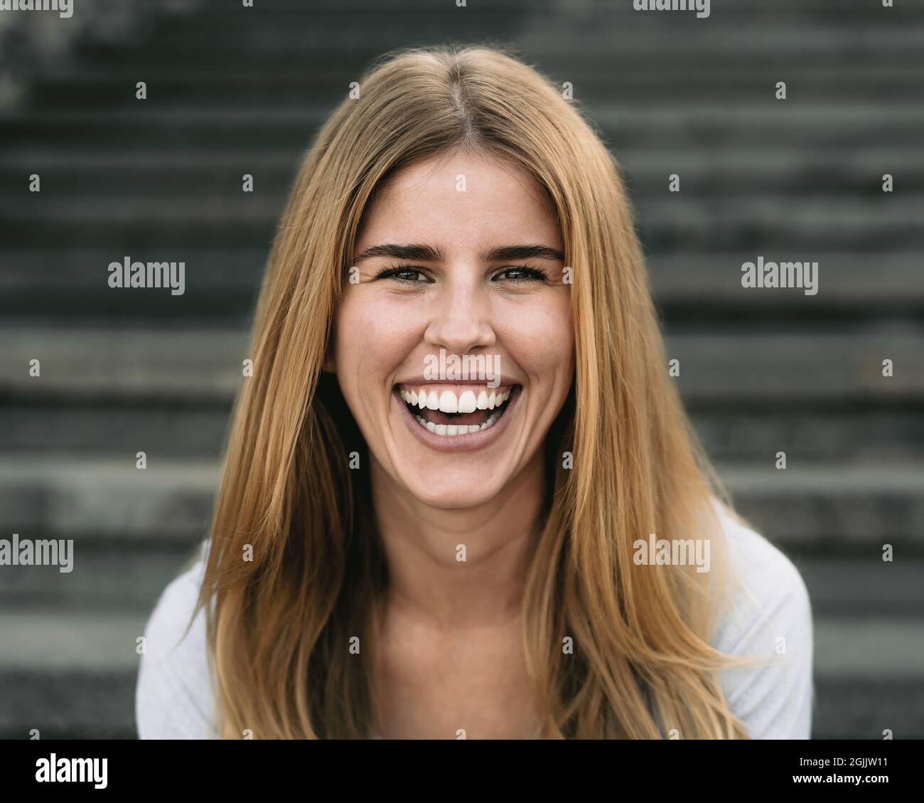 Happy young woman smiling into the camera while sitting on urban stairs ...