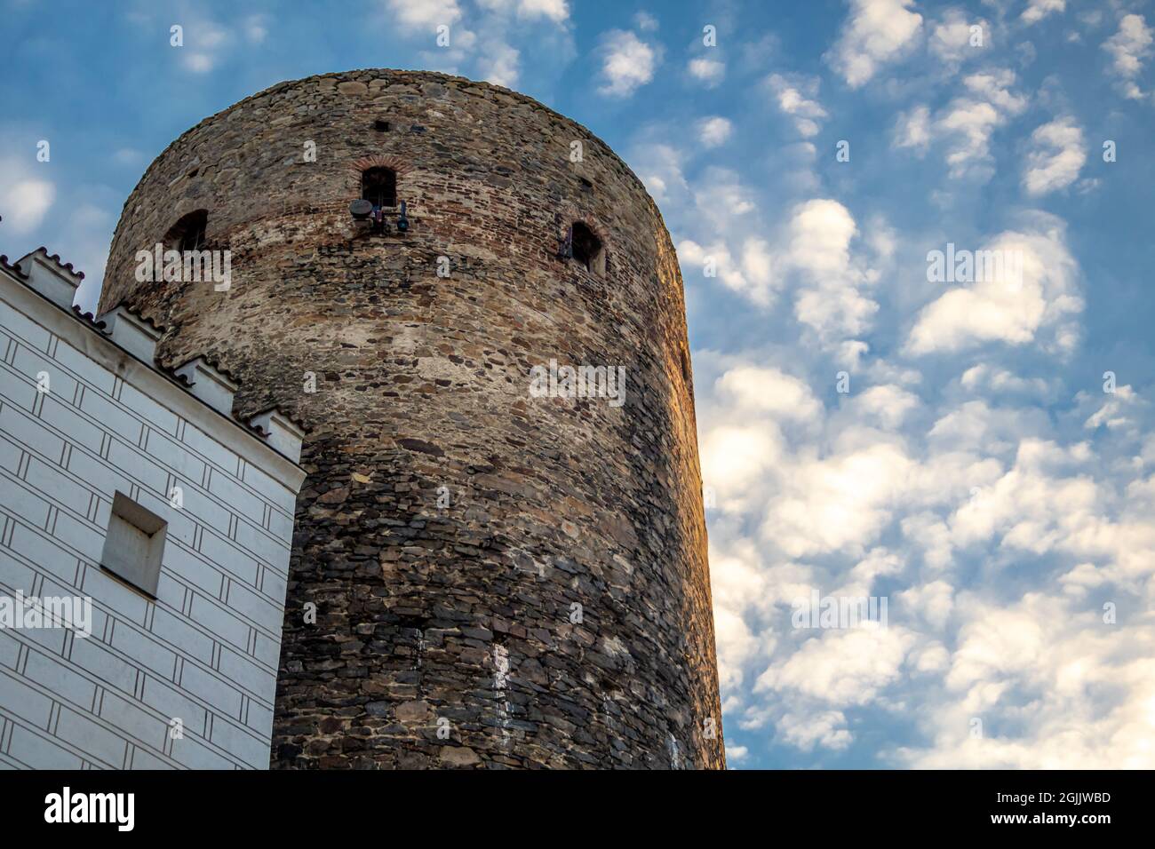 View up to an old brick fortified tower and house with white facade in front of blue sky with white clouds in evening light Stock Photo