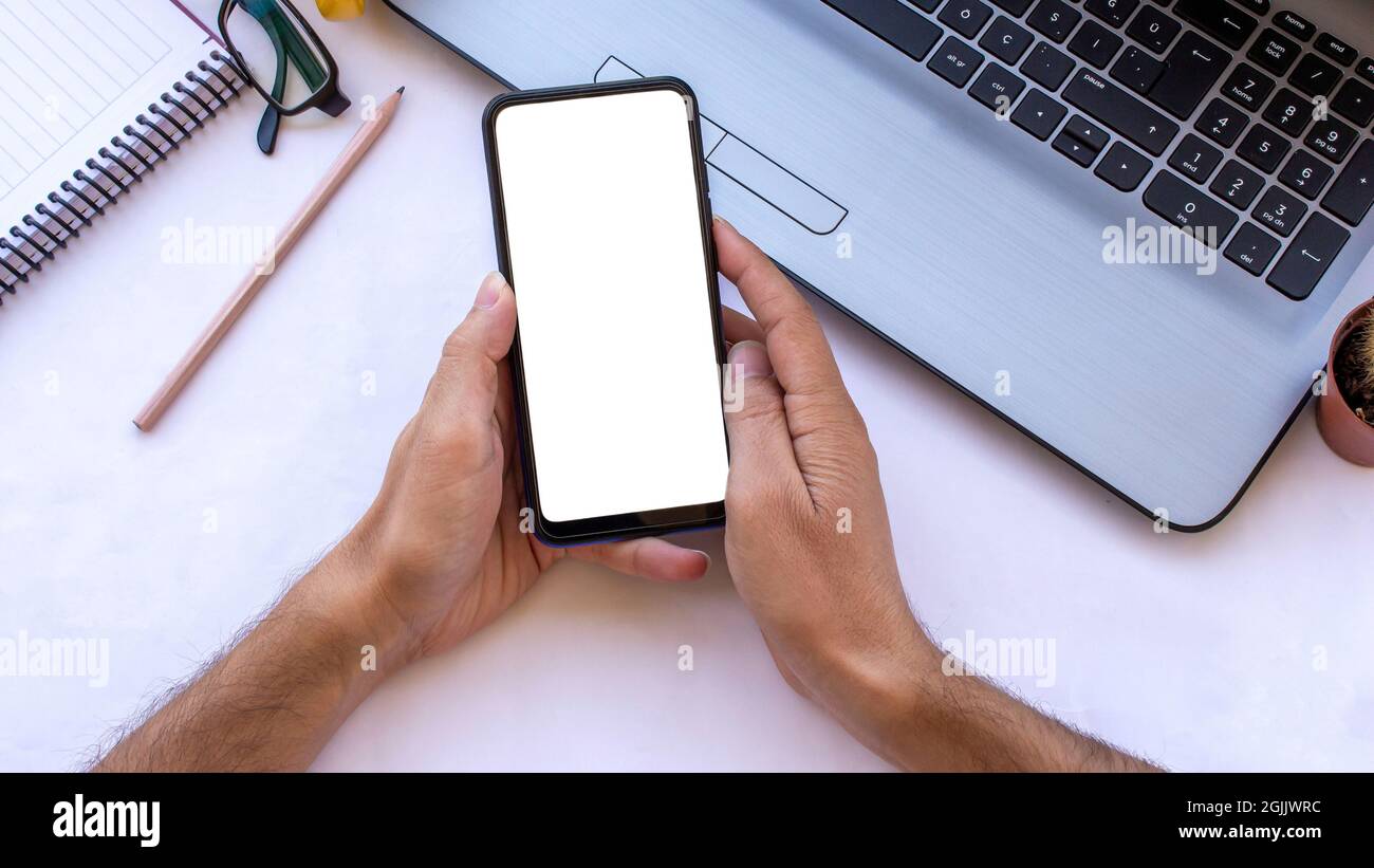 Mockup image of man hand using blank white desktop screen mobile phone on office desk. Stock Photo