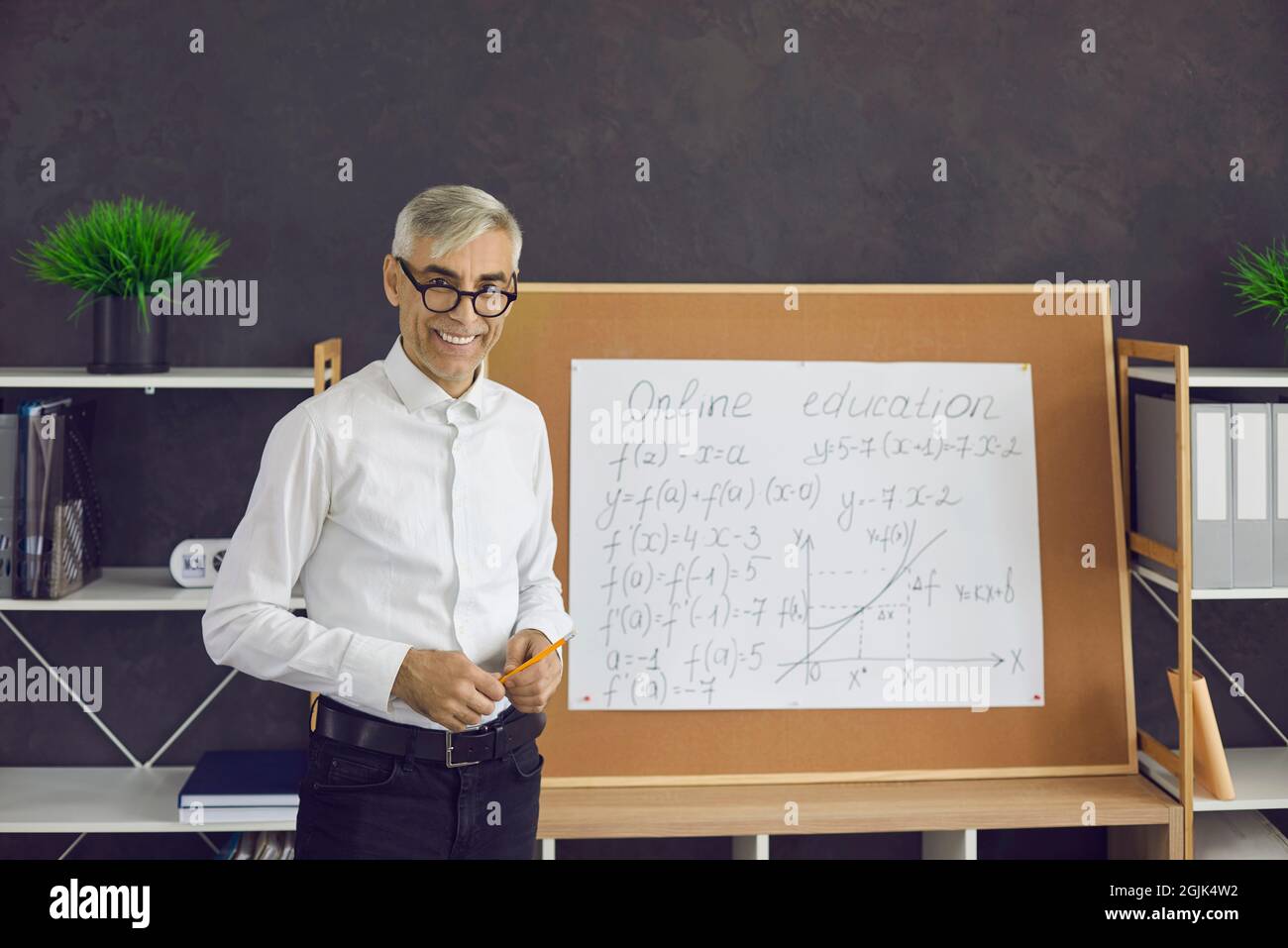 Portrait of a friendly senior male teacher who remotely conducts a math lesson for his students. Stock Photo