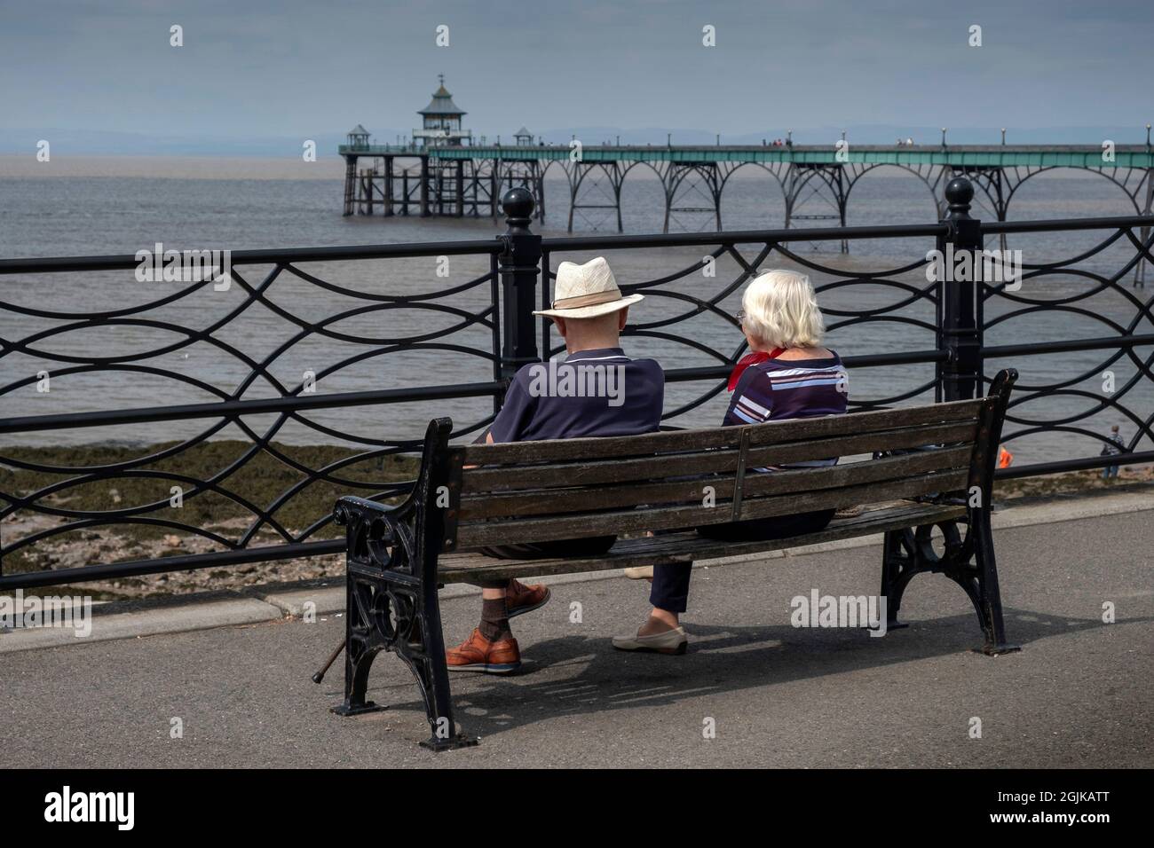 An elderly couple sitting on a bench with a view of Clevedon Pier Stock Photo