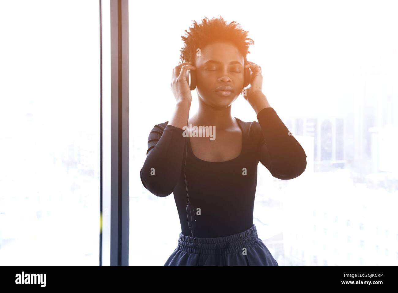 An African-American woman listens to music with headphones. A young woman in a sports uniform on the background of a window. High quality photo Stock Photo