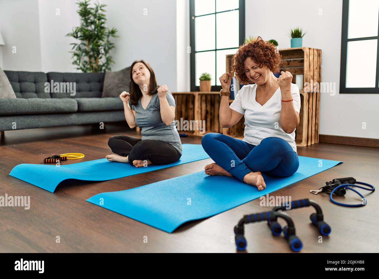 Family of mother and down syndrome daughter doing exercise at home very happy and excited doing winner gesture with arms raised, smiling and screaming Stock Photo