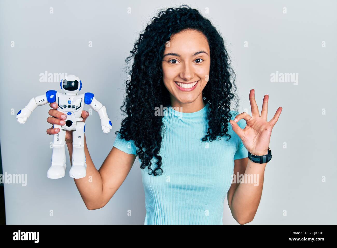 Young hispanic woman with curly hair holding robot toy doing ok sign with  fingers, smiling friendly gesturing excellent symbol Stock Photo - Alamy