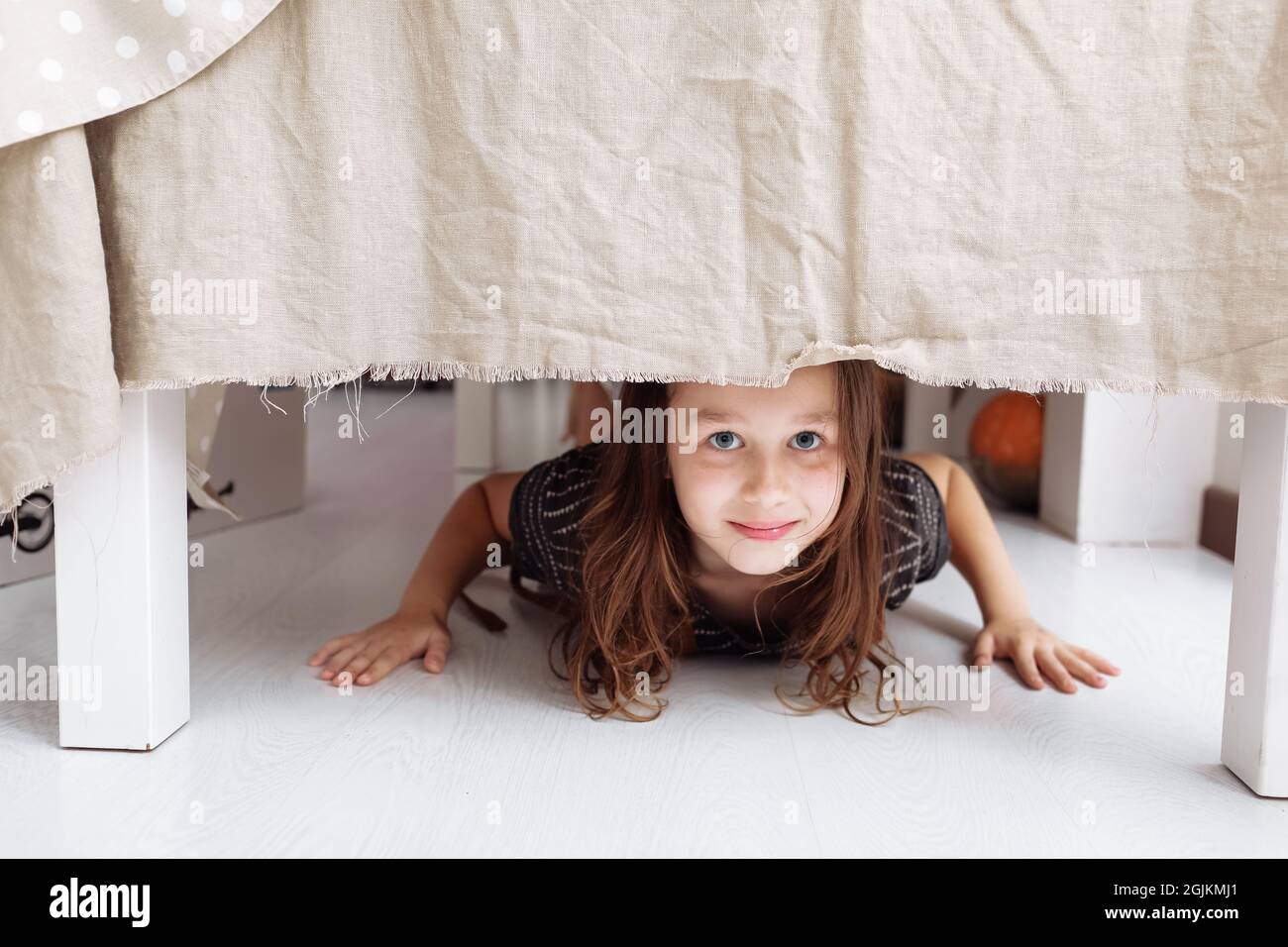 portrait-of-cute-small-girl-lying-on-floor-under-table-indoors-at-home-looking-at-camera-2GJKMJ1.jpg