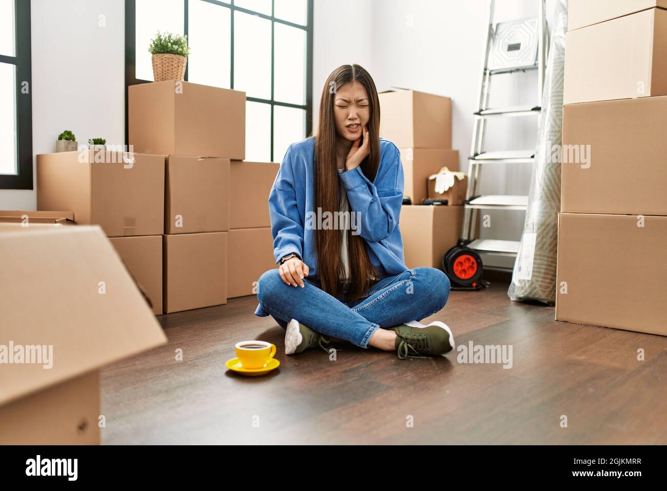 Young chinese girl sitting on the floor at new home touching mouth with ...