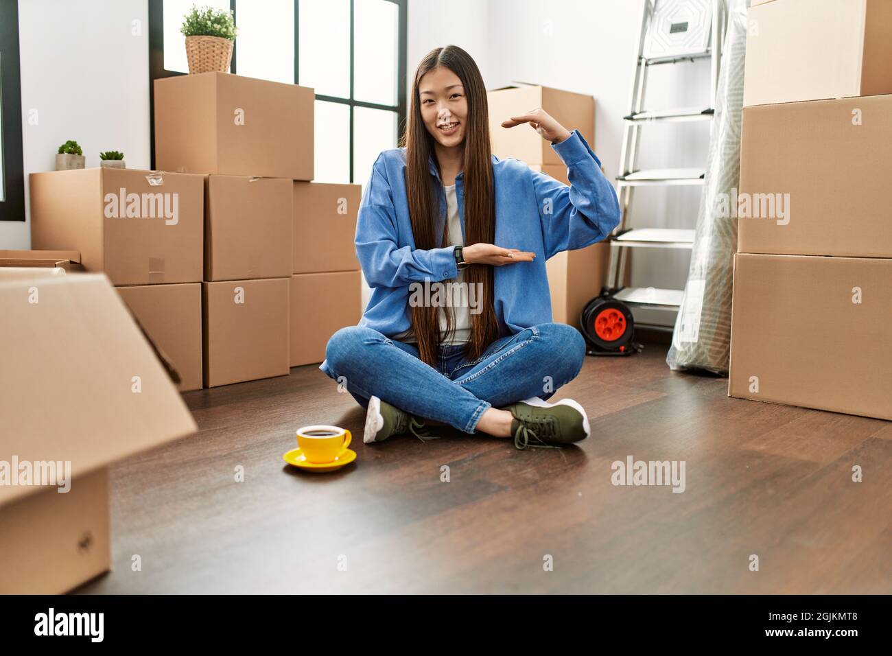 Young chinese girl sitting on the floor at new home gesturing with ...