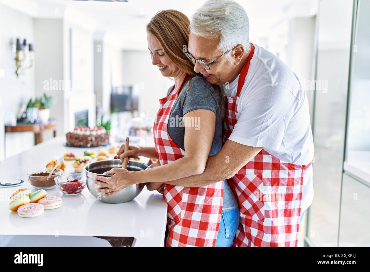 Middle age hispanic couple smiling happy and hugging cooking sweets at ...