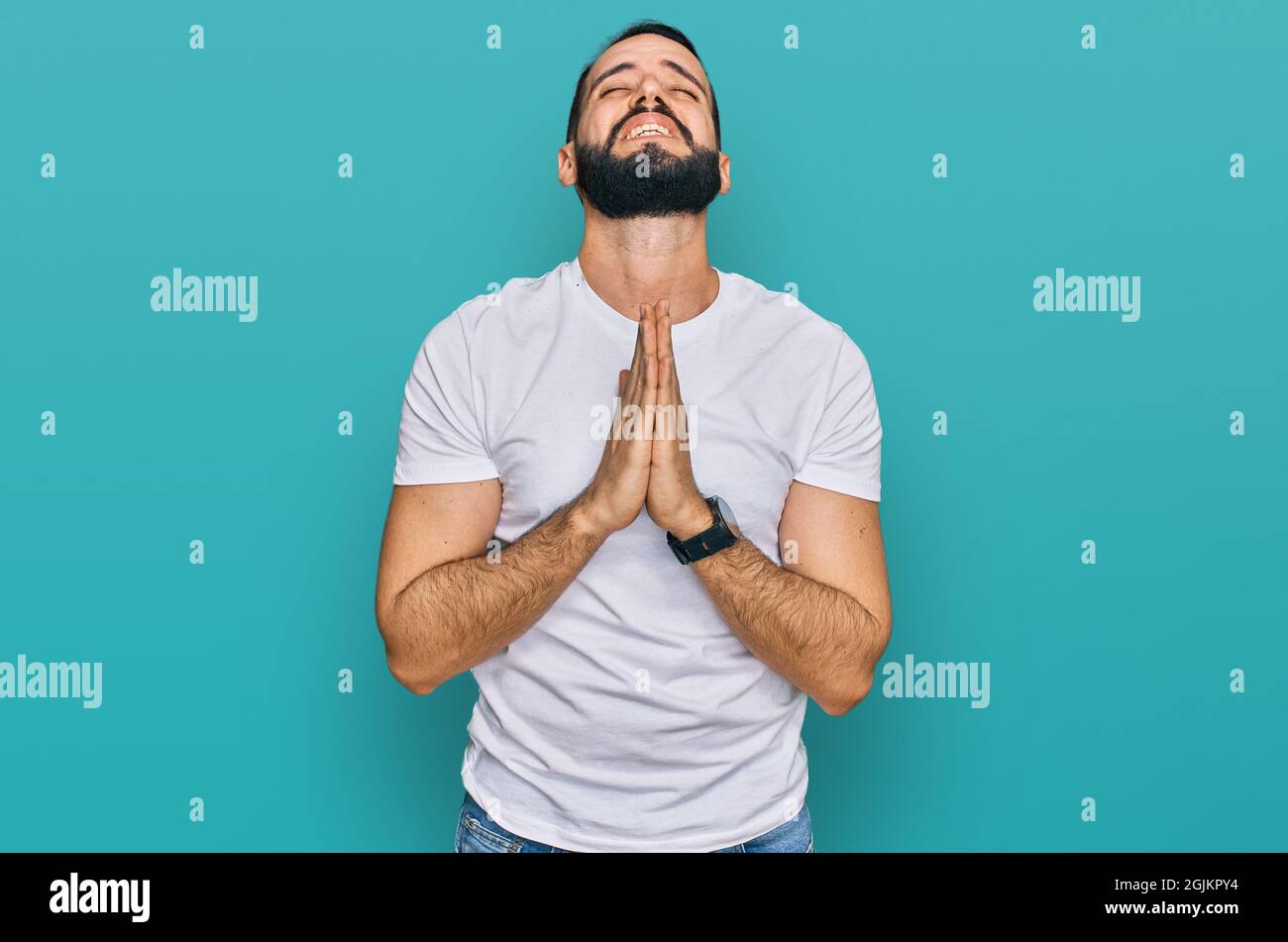 Young man with beard wearing casual white t shirt begging and praying ...