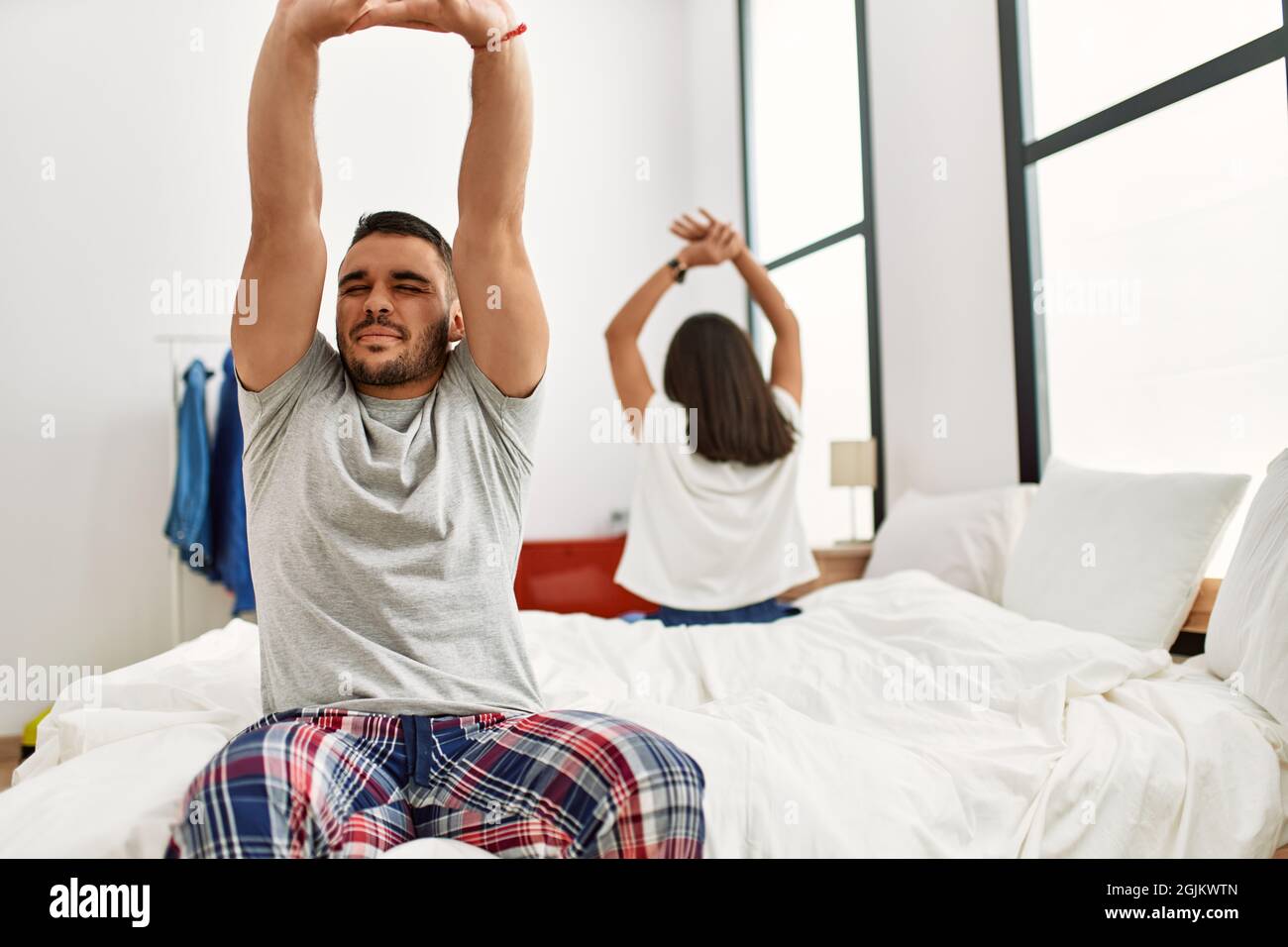 Young latin couple yawning and stretching arms sitting on the bed Stock