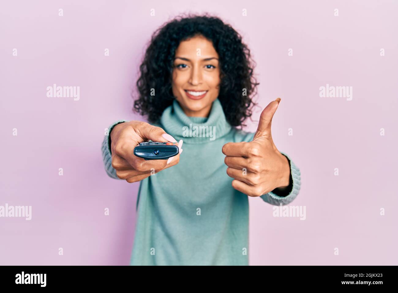 Young latin girl holding television remote control smiling happy and ...