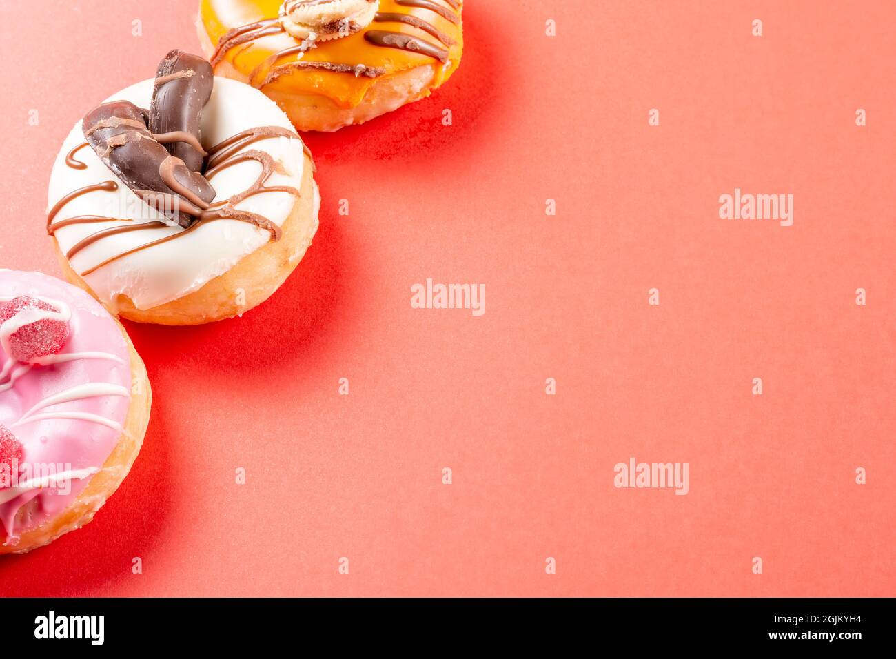 Photo of a white chocolate donuts and two half colored donuts on a red background.The photograph has copy space and is taken in horizontal format. Stock Photo