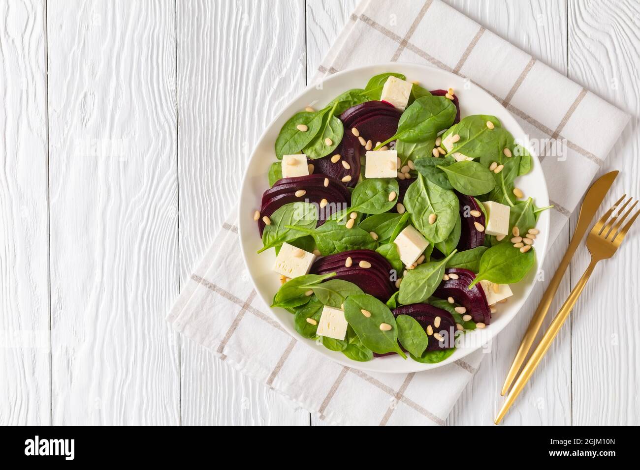 roasted beet salad with cubed feta cheese, pine nuts and spinach on a white plate with golden cutlery on a wooden table, canadian cuisine, flat lay, f Stock Photo