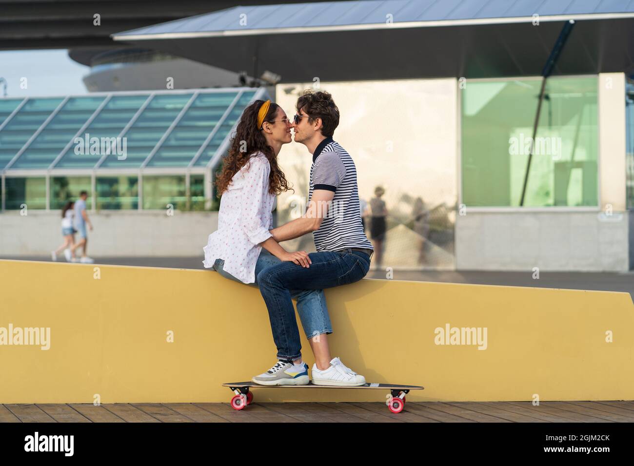 Stylish couple kissing sitting in skatepark. Young cute longboarders man and woman in love cuddling Stock Photo