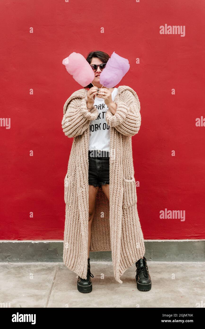 Vertical image of a woman with two cotton candy, pink and lilac. Funny image of a woman standing in the street looking at the camera with sunglasses, Stock Photo