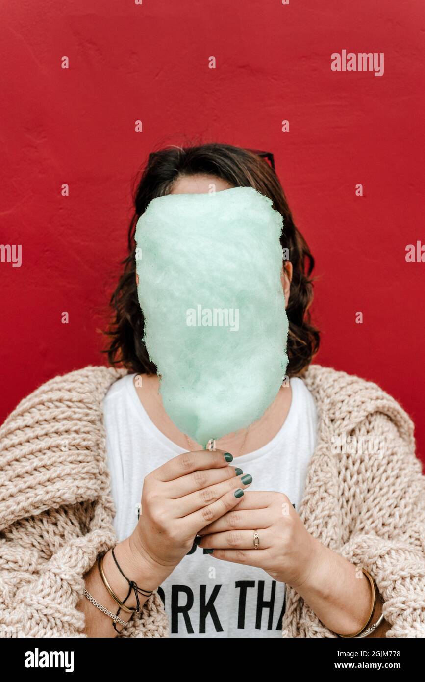 Vertical image of an unrecognizable girl who covers her face with a little green sugar, wears a light handmade sweater and paints her nails green. Cop Stock Photo
