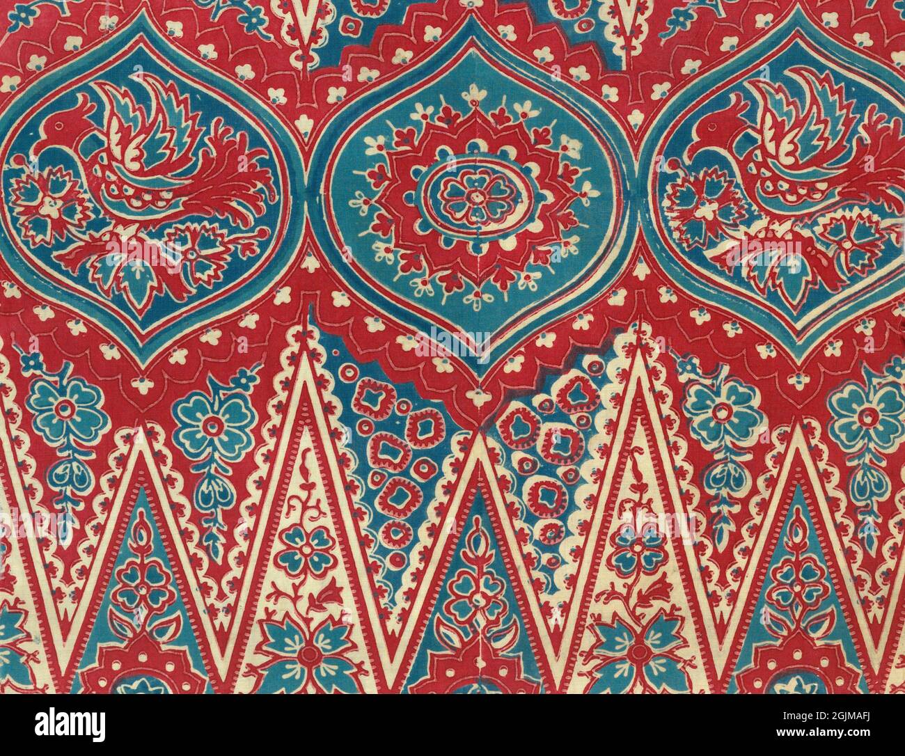 Indonesian red and blue batik cotton textile. Row of three ogival medallions: middle one with rosette, outer two with crested bird and flowers as well as remnants of deep toothed zigzag border below. Indonesia Stock Photo