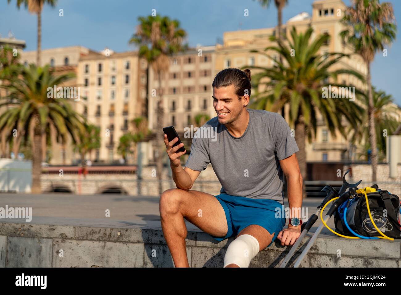 Young latin man with crutches using mobile phone after doing exercise Stock Photo