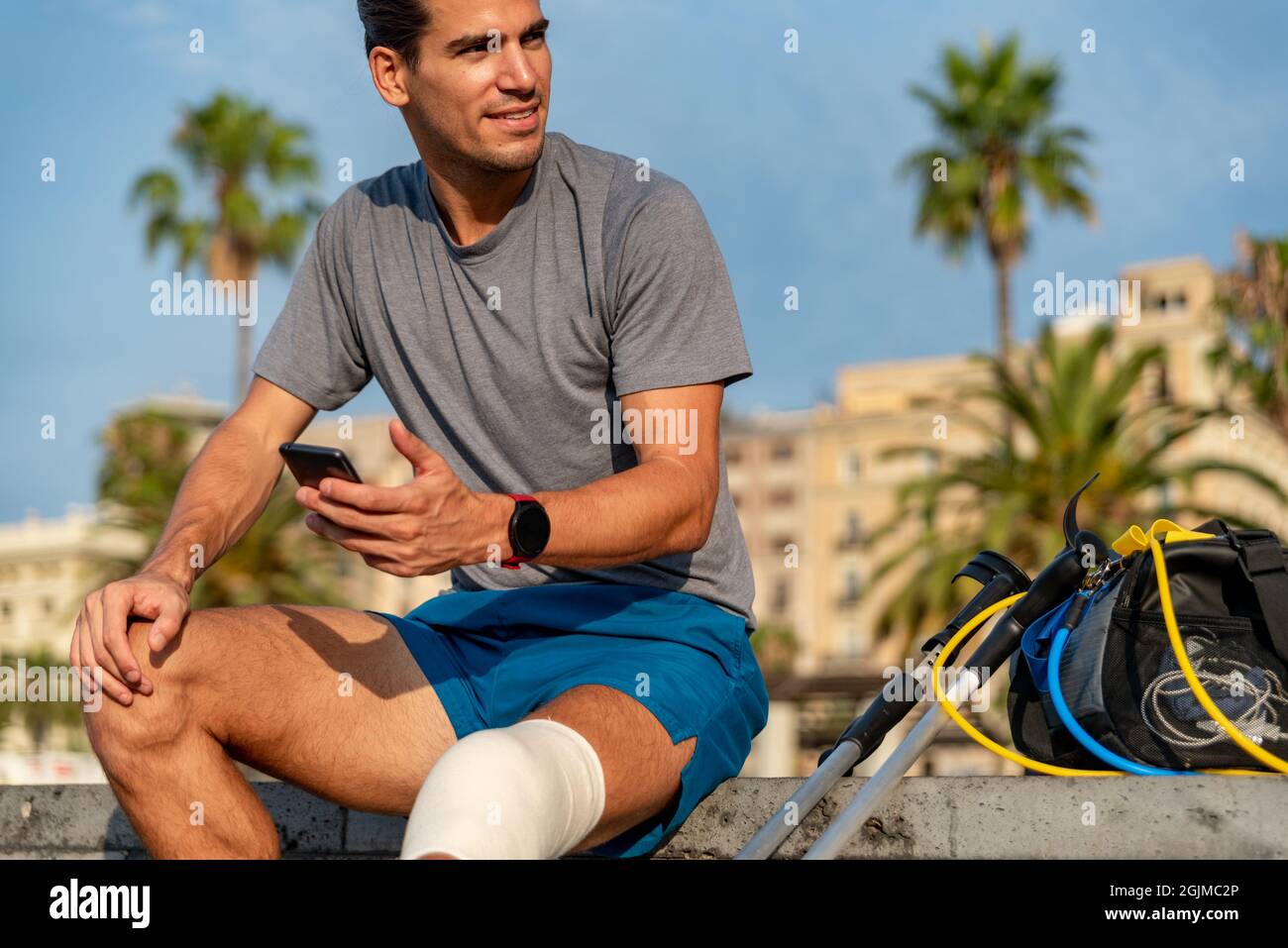 Young latin man with crutches using mobile phone after doing exercise Stock Photo