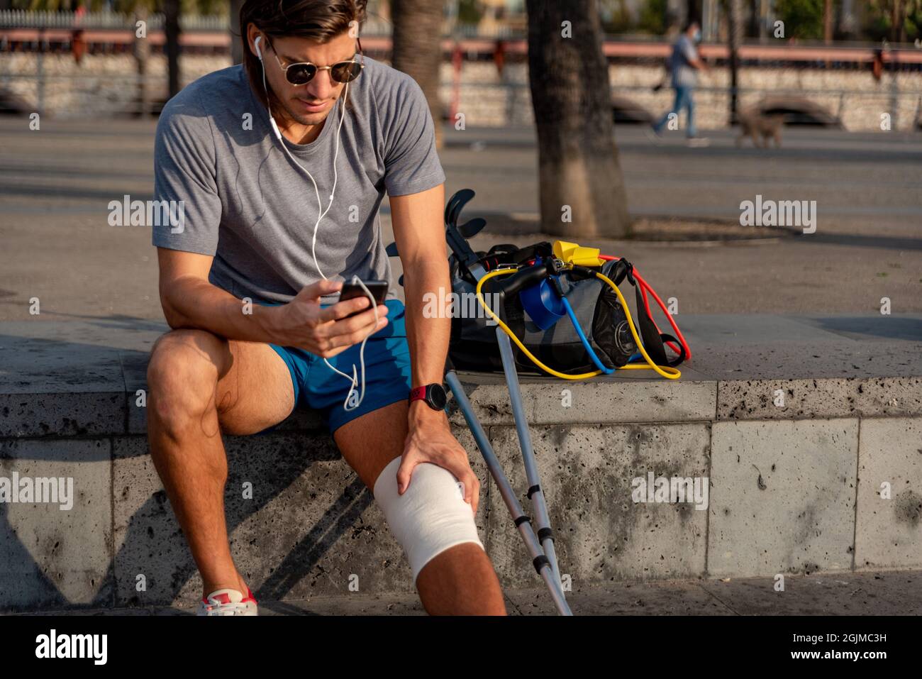 Young latin man with crutches using mobile phone after doing exercise Stock Photo