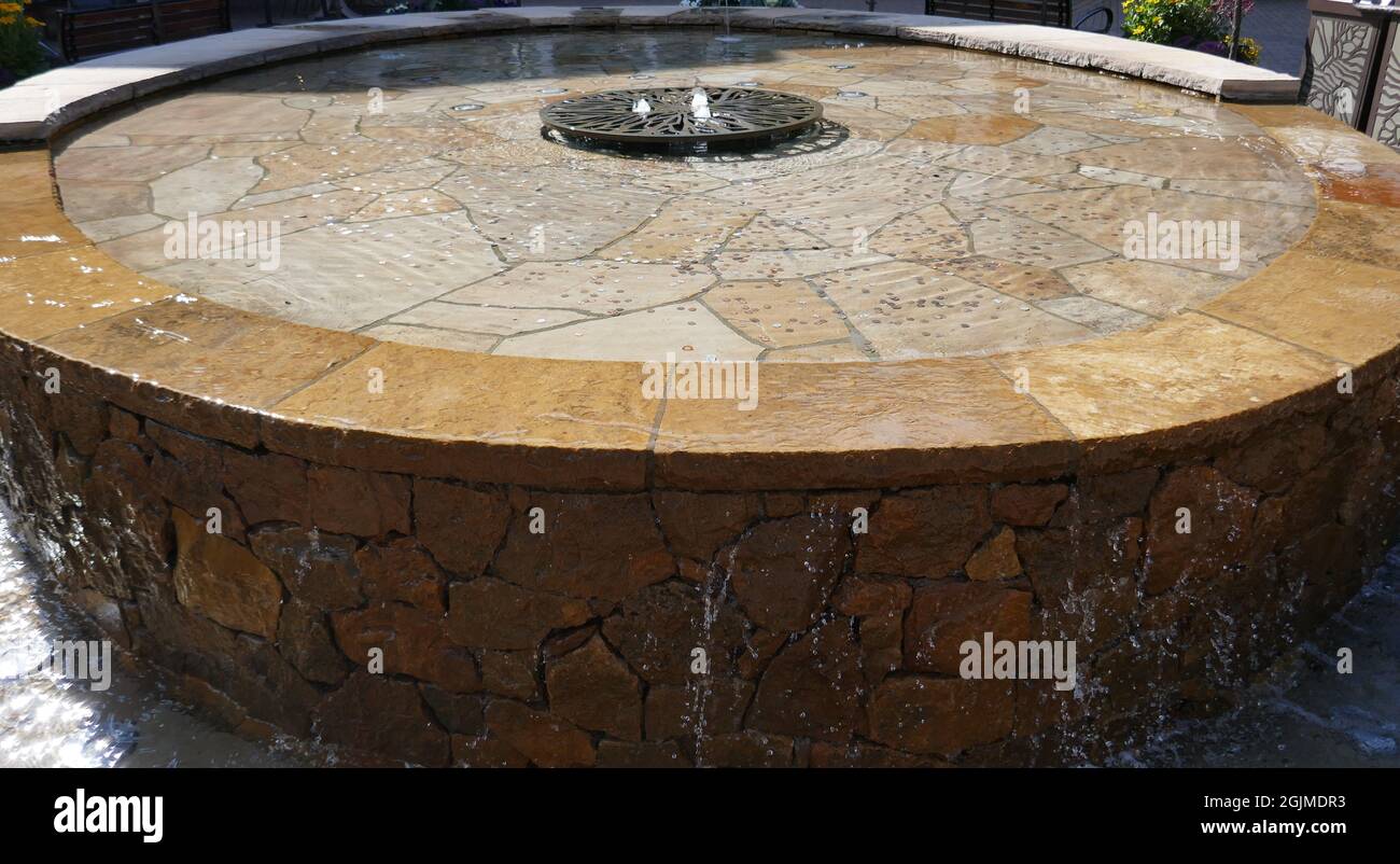 Round water fountain pool with water running over stone sides Stock Photo