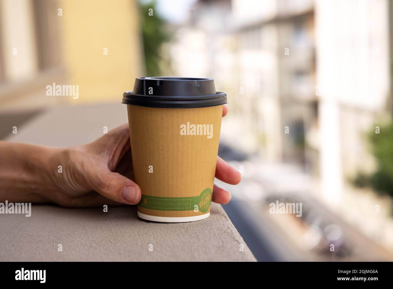 Hands holding a single use paper coffee cup. Young woman in a balcony ...