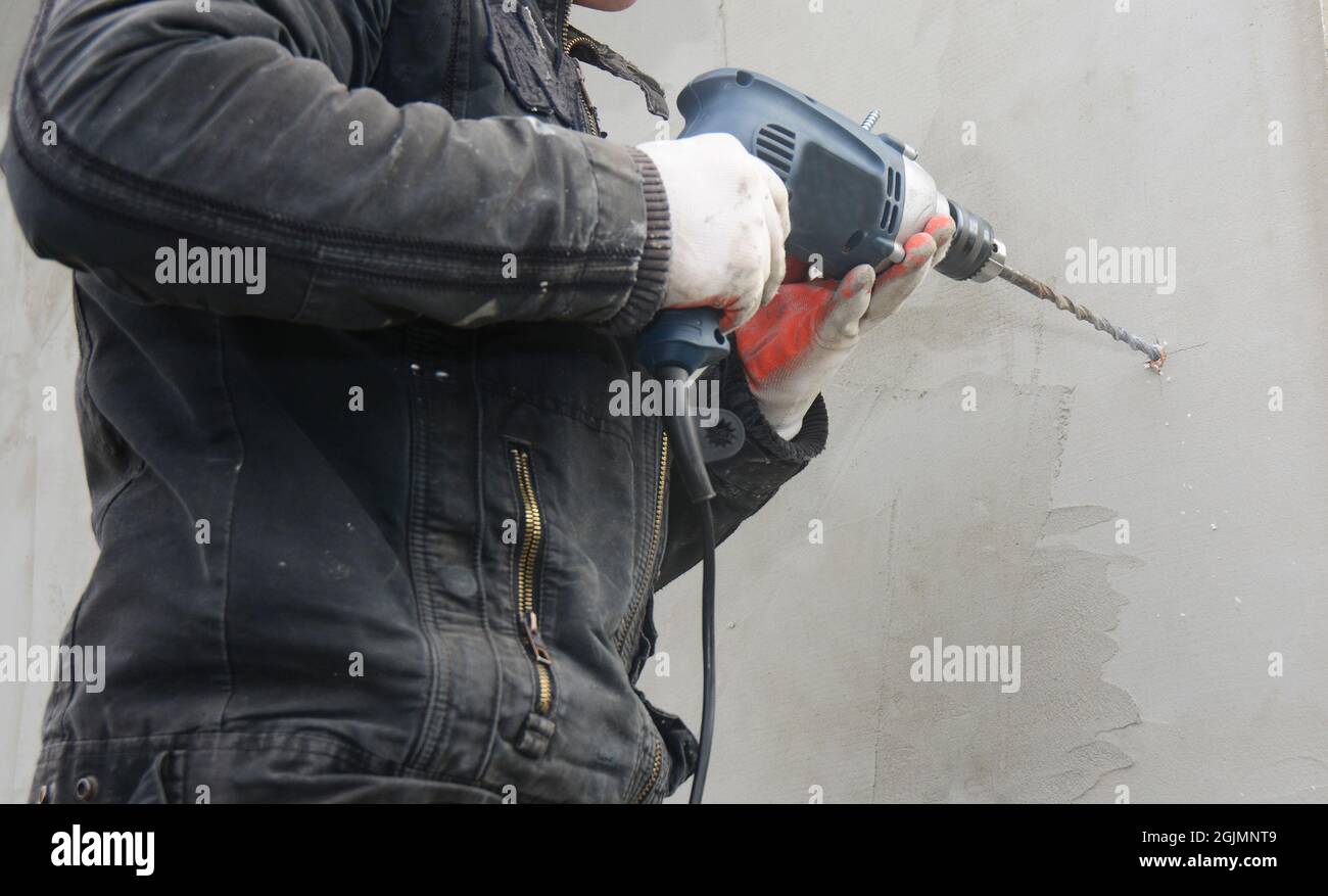 Contractor drilling plaster wall to install rain gutter downspout pipe