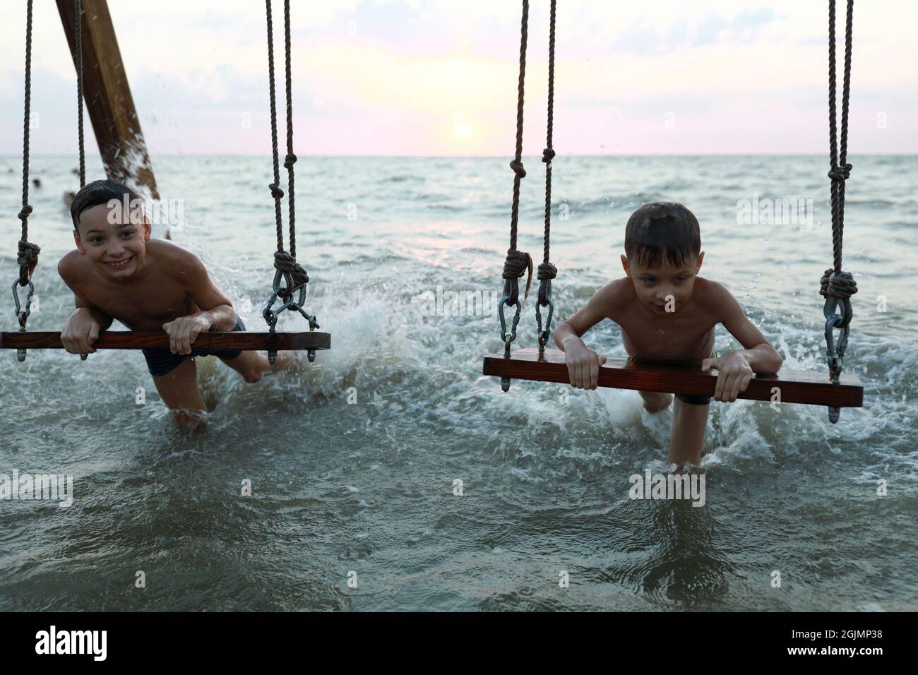 Azov Boys Boys swinging on swing in Sea of Azov at sunset Stock Photo - Alamy