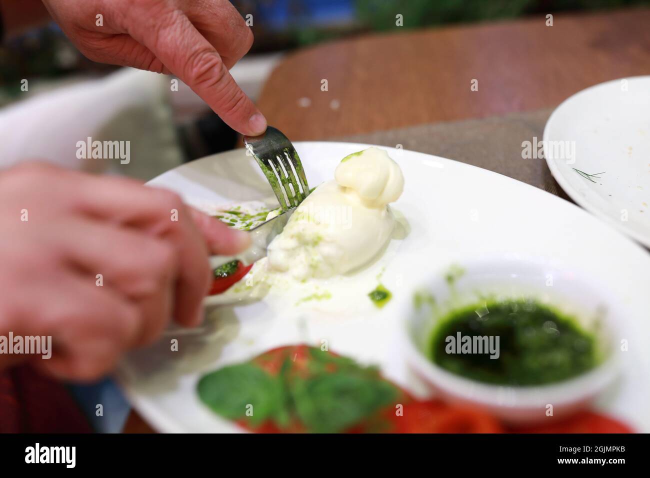 Person cutting Burrata cheese on plate in restaurant Stock Photo Alamy