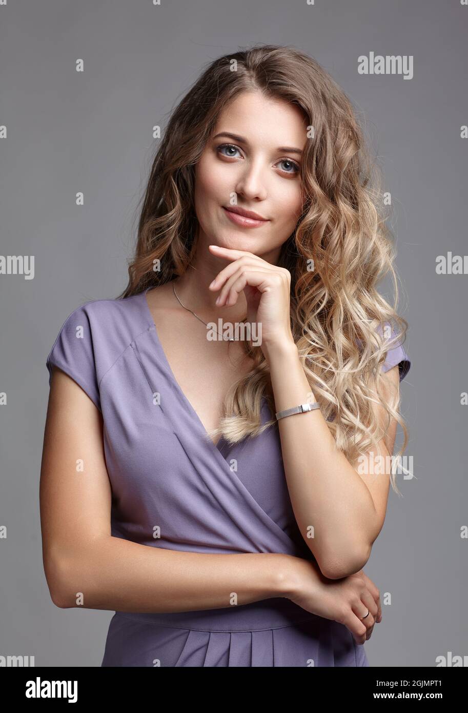 Studio beauty portrait of a young woman in a summer dress. Blond female in a summer dress posing over gray background. Girl with hand near face. Stock Photo