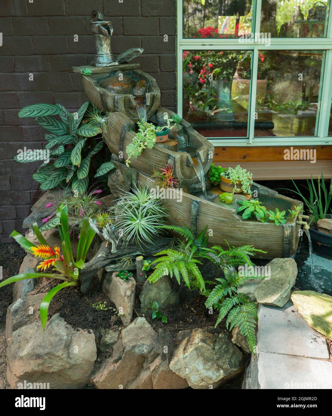 Unusual water feature with waterfall, created from old beer kegs, trickling into pond and bordered by rockery with ferns and bromeliads, in Australia Stock Photo