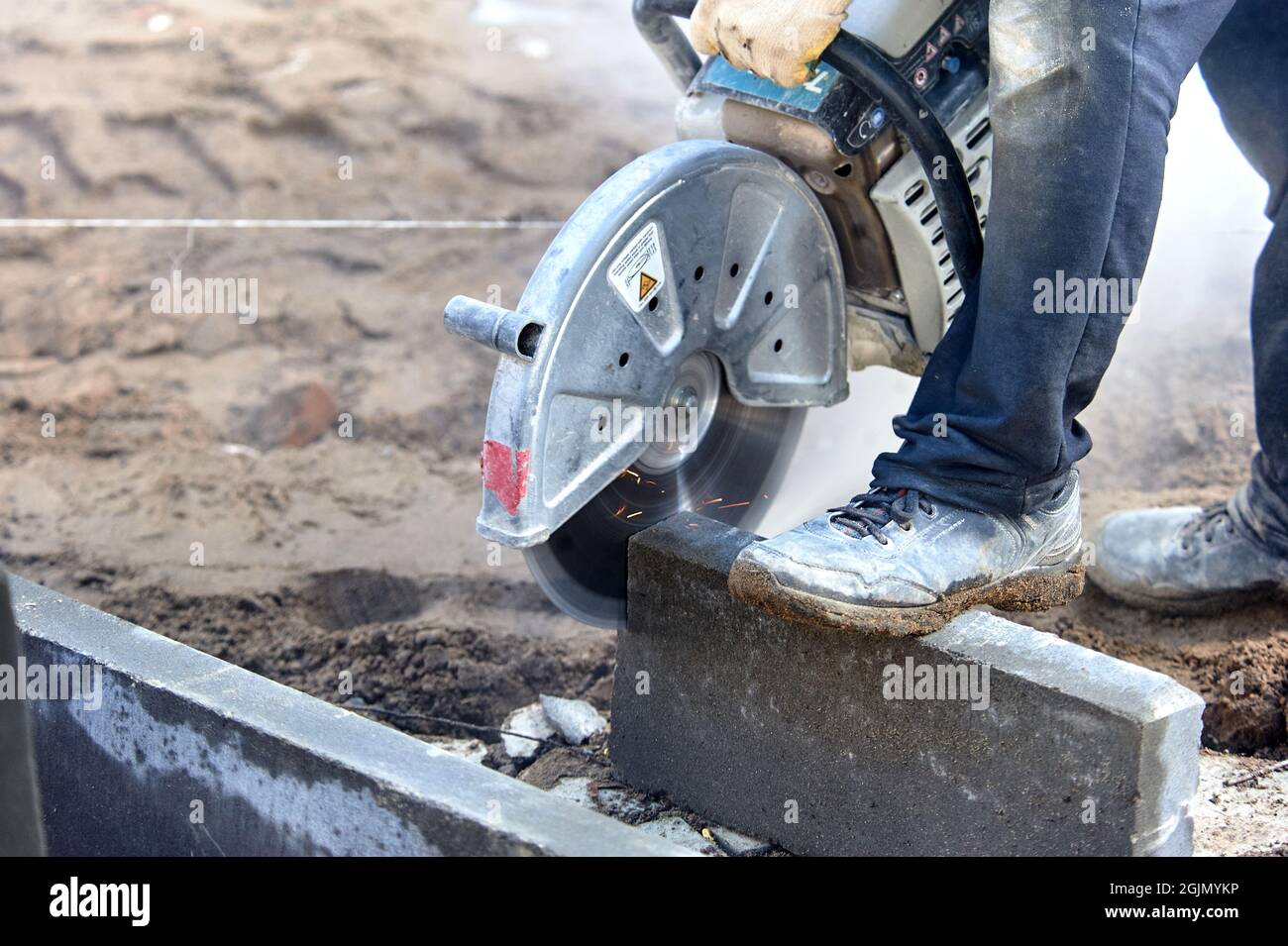 A worker with a circular saw cuts a curb stone close-up. Stock Photo