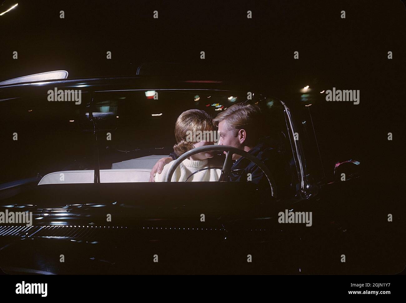 USA in the 1960s. A young couple in a convertible at night. They are sitting close together in the front seat of the car. Kodachrome slide original.   Credit Roland Palm ref 6-9-16 Stock Photo
