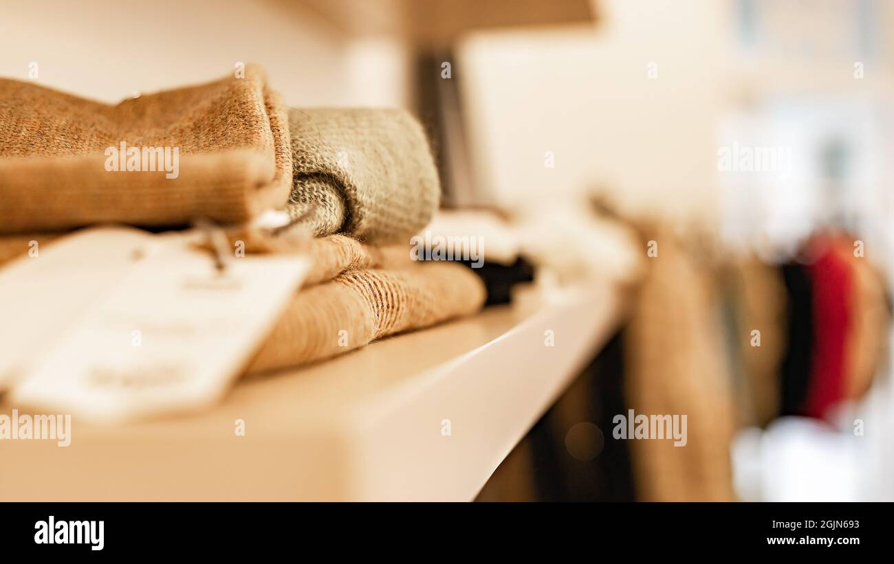 Knitted dresses and beige jumpers are on the shelf. Fashionable women's clothing. Branded clothing in a show room. Fashion retail, show room, shopping Stock Photo