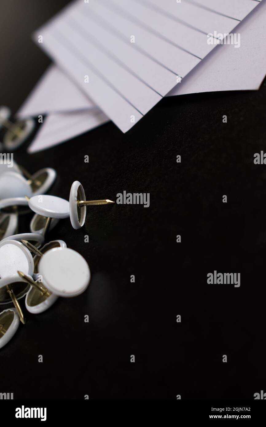 Vertical shot of white drawing pins and papers on a black surface Stock Photo